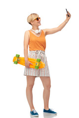 sport, leisure and skateboarding concept - smiling teenage girl with short modern cruiser skateboard taking selfie by smartphone over white background