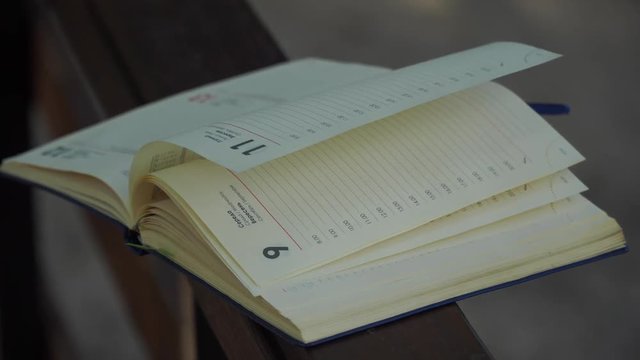 Wind turns the pages of open Notebook lies on wooden handrail in park, business concept