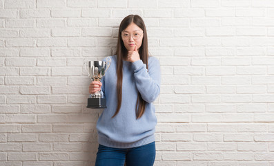 Young Chinese woman holding trophy serious face thinking about question, very confused idea