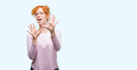 Young redhead woman afraid and terrified with fear expression stop gesture with hands, shouting in shock. Panic concept.