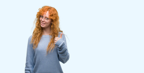 Young redhead woman wearing glasses happy with big smile doing ok sign, thumb up with fingers, excellent sign