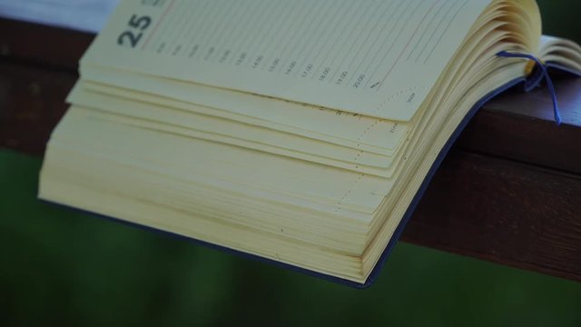 Wind turns the pages of open Notebook lies on wooden handrail in park, business concept