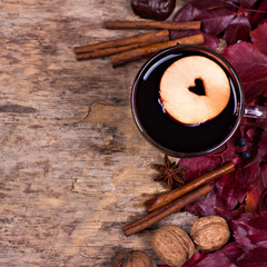 Hot Mulled wine with spices and fruits on an old wooden background. Autumn leaves, nuts, cinnamon. Autumn background. Text space.