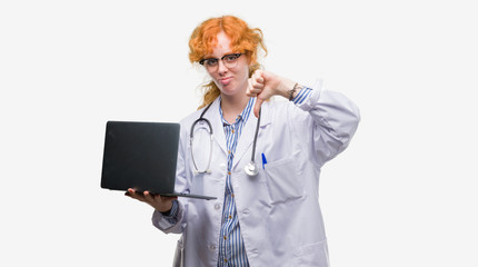 Young redhead doctor woman holding computer laptop with angry face, negative sign showing dislike with thumbs down, rejection concept