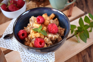 Porridge with apples, raspberries and honey topped with mint. Healthy breakfast meal