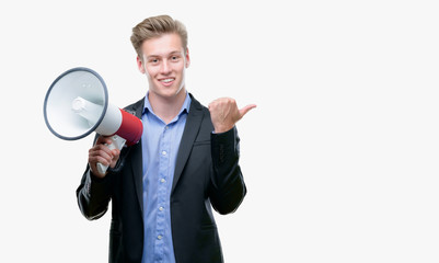 Young handsome blond man holding a megaphone pointing with hand and finger up with happy face...