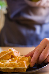 woman hands prepare waffle for serving process.waffle made from dough and batter.tasty dessert sweets waffle served on daylight in cafe background.waffle on black plate.