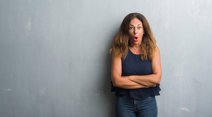 Fototapeta na wymiar Middle age hispanic woman standing over grey grunge wall afraid and shocked with surprise expression, fear and excited face.