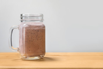 Berry smoothie in a mason jar on a wooden cutting board.