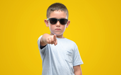 Dark haired little child wearing sunglasses pointing with finger to the camera and to you, hand...