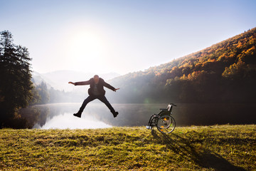 Senior man jumping by the wheelchair in autumn nature.