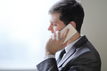 close up.businessman talking on smartphone while standing near an office window