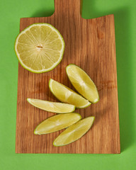 Slices and half of natural ripe green lime on a wooden board on a green background. Top view.
