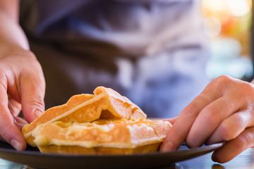 woman hands prepare waffle for serving process.waffle made from dough and batter.tasty dessert sweets waffle served on daylight in cafe background.waffle on black plate.
