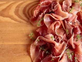 Italian prosciutto crudo or jamon with thyme on a wooden table.