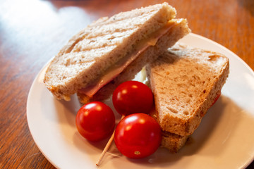 Simple yet tasty and delicious sandwich made with whole wheat bread and cold cuts with dressing, garnish with fresh red tomatoes. A healthy choice snack or light lunch. Selective focus. Natural light.