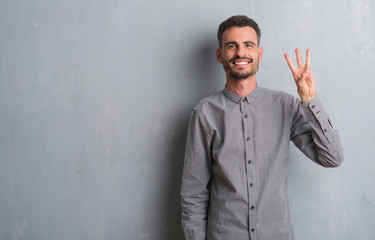 Young adult man standing over grey grunge wall showing and pointing up with fingers number three...
