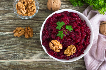 Boiled beetroot with nuts in a white bowl on a wooden background. Top view.