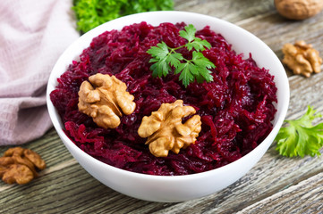 Boiled beetroot with nuts in a white bowl on a wooden background.