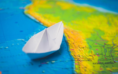 Trip around the world. White paper boat and colorful world map
