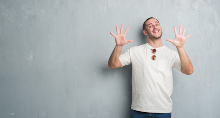 Young caucasian man over grey grunge wall wearing sunglasses showing and pointing up with fingers...