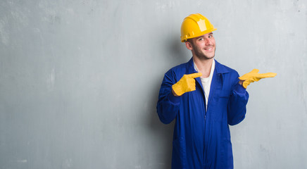 Young caucasian man over grey grunge wall wearing contractor uniform and safety helmet very happy...