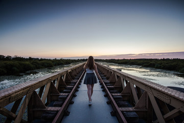 A happy young slender girl walks near a bridge in the rays of the summer sun.