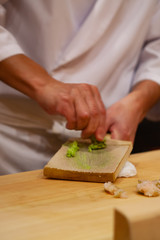 Obraz na płótnie Canvas Professional sushi chef is using Oroshigane to grate fresh root of Wasabi or Japanese horseradish. Oroshigane or oroshiki is a Japanese style hand grater with the surface made from shark skin.