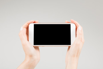 Female holding white smartphone with blank screen in two hands hand