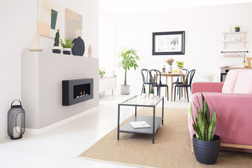 Real photo of bright Nordic living room interior with dining table, pink lounge and metal coffee...