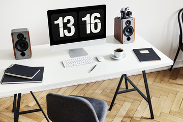 High angle of a desk with a computer, notebooks, speakers and keyboard next to a chair in a home office interior. Real photo