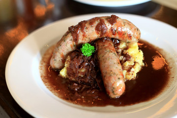 Closeup German Pork Sausages and Mashed Potatoes with parsley and sauce in the white plate on the wooden table. Foods concept.