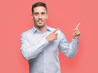 Handsome young businessman smiling and looking at the camera pointing with two hands and fingers to...