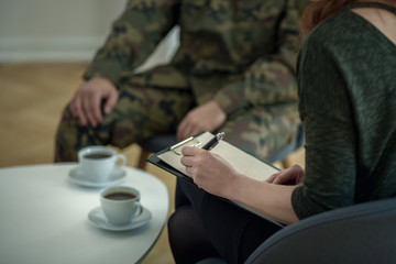 Close-up of psychologist writing down notes while talking to her patient from army