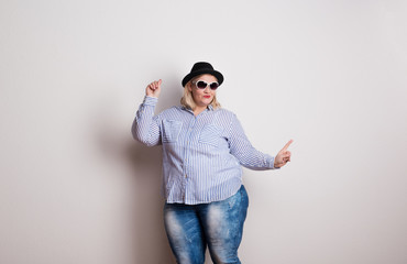 Portrait of an attractive overweight woman with hat and sunglasses in studio.