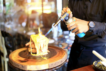 Chef cooking of Crispy Fried Chicken Lava Cheese on wooden board background in the restaurants, with the man hand spraying the blow torch into the hot cheese. Foods concept. Warm lights tone.