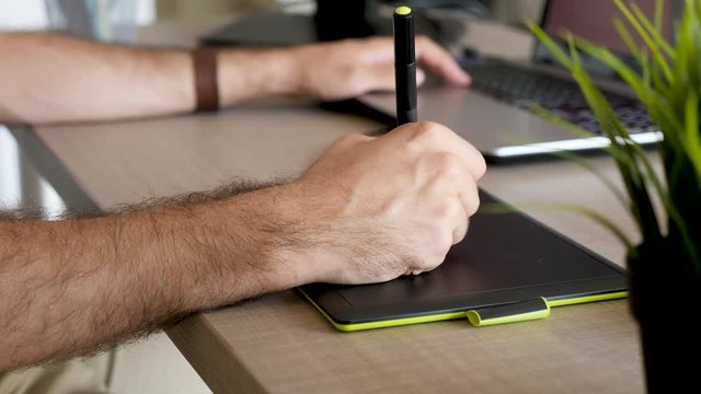 Man hand drawing using a digitiser digital tablet ot his desk. Creative professional. Close up footage