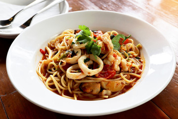 Fresh Spaghetti Spicy Seafood with squid, prawn, mussel, in the white plate on wooden table background. Foods concept.