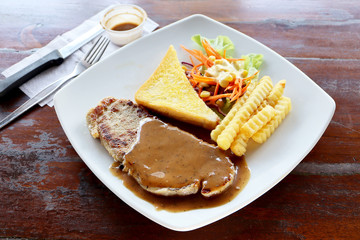 Beef Steak set with black pepper sauce on white plate, Potato or french fries and bread and some vegetable salad on wooden table background, as foods concept.