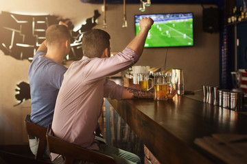 Two friends watching football game and drinking beer