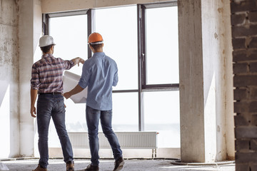 engineer is showing the execution of building project to a customer indoors. full length photo