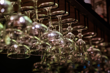 Empty cocktail and wine glasses on bar interior background. Artificial lighting creates reflections and glares in glass. Selective focus in center of image.