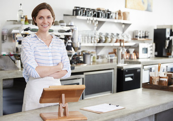 Smiling woman behind counter at a coffee shop, arms crossed