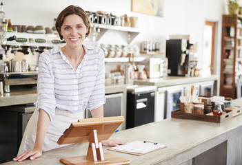 Young female owner leaning on the counter at her coffee shop