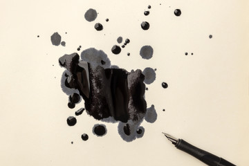An overhead photo of drops of ink and a nib pen, with copy space