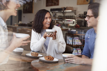 Three young adult friends talking, drinking coffee at cafe
