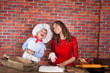 Cheerful mother and her little son preparing dough in the kitchen