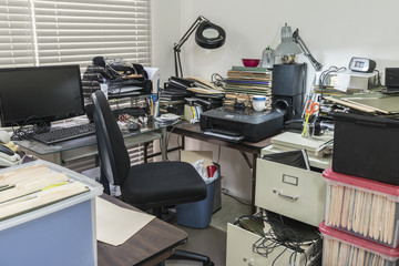 Messy business office desk with boxes of files and disorganized clutter.