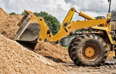 Yellow tractor loader is picking up a bucket of earth, mechanical, ladle with earth