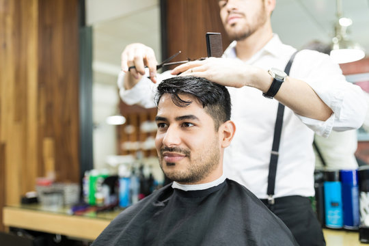 Man Looking Away While Getting Haircut From Barber At Shop